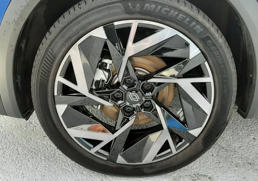 Gros plan sur la roue avant droite du Renault Captur bleu iron, jante alliage noire et argent au design géométrique.