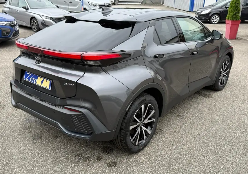 Vue 3/4 arrière droite d’un Toyota C-HR gris atlas 2025 avec feux arrière LED et jantes alliage noires et argentées.