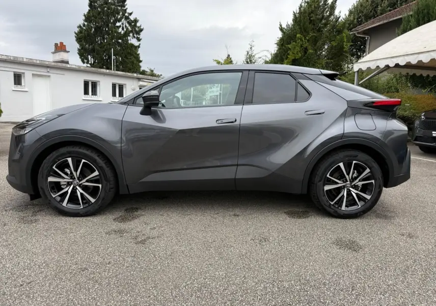 Profil côté gauche du Toyota C-HR 1.8 140CH STYLE 2025 en gris atlas avec jantes alliage noires et argentées.