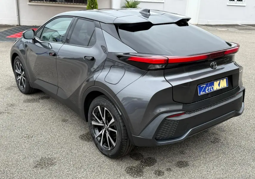Toyota C-HR 1.8 140CH STYLE 2025 gris atlas vu en 3/4 arrière droit avec feux arrière LED continus et jantes alliage.