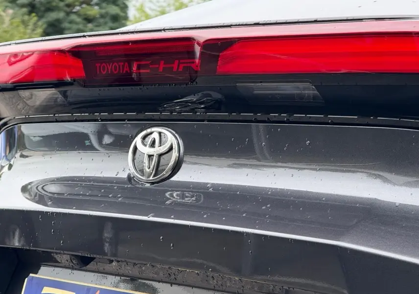 Gros plan arrière sur le hayon gris atlas du Toyota C-HR 1.8 140CH STYLE MY25 avec logo et feu stop rouge intégré.