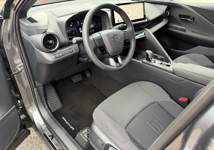 Intérieur avant gauche du Toyota C-HR gris atlas 2025, volant multifonction et écran tactile central visible.