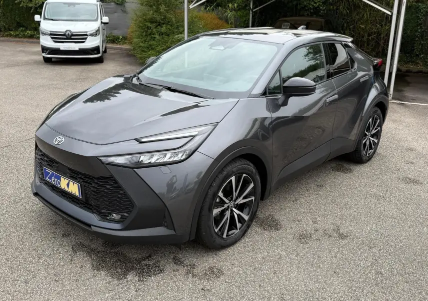 Toyota C-HR 1.8 140CH STYLE gris atlas en 3/4 avant droit avec jantes noires et toit panoramique.
