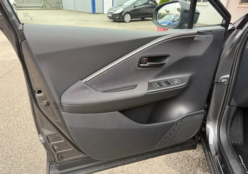 Porte avant gauche ouverte d’un Toyota C-HR gris atlas 2025, montrant les commandes de vitres et la garniture intérieure.