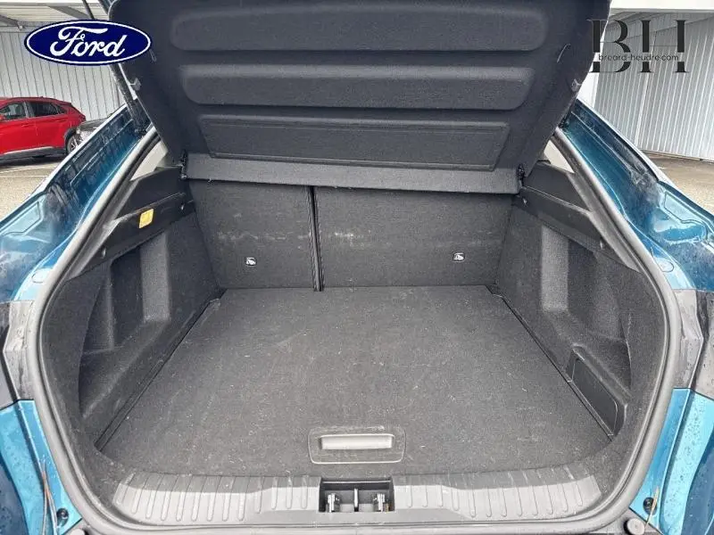 Coffre ouvert en vue arrière d'une Renault Arkana Bleu Zanzibar, montrant l'espace de chargement vide et la moquette noire.