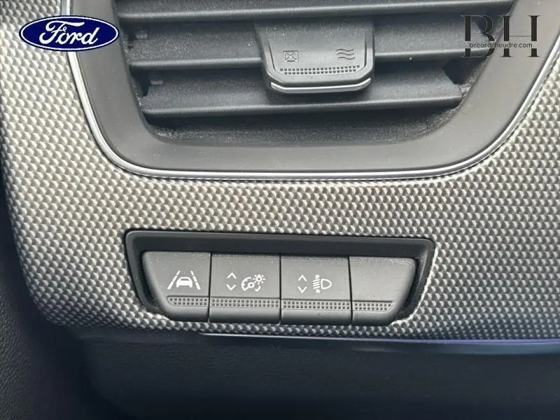 Gros plan sur les commandes d'assistance à la conduite intégrées dans le tableau de bord gris texturé du Renault Arkana Bleu Zanzibar.