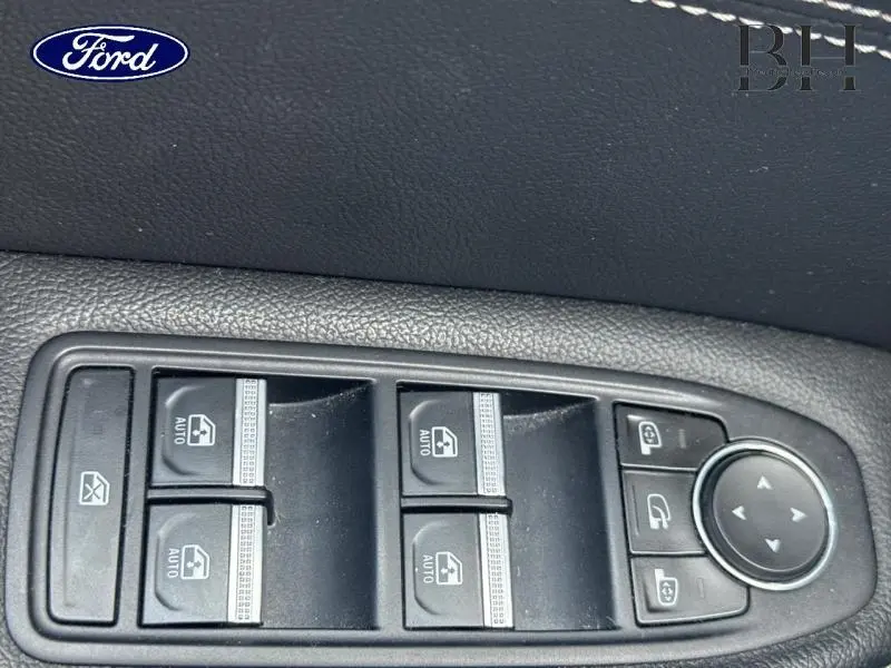 Gros plan sur les commandes des vitres électriques et des rétroviseurs d'une Renault Arkana Bleu Zanzibar, intérieur noir.