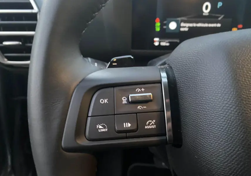 Gros plan sur les commandes multifonctions gauche du volant noir d'une Citroën C4 2025, avec affichage numérique en arrière-plan.