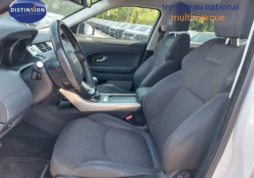 Intérieur du Range Rover Evoque blanc 2018, vue côté conducteur, sièges noirs et tableau de bord moderne.