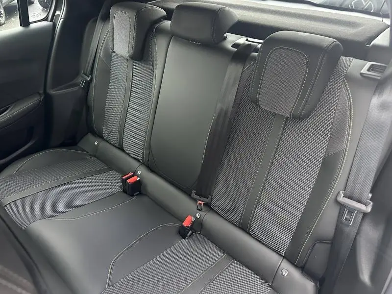 Vue intérieure sur les sièges arrière noirs et gris texturés du Peugeot 208 Hybrid 2025 avec ceintures de sécurité visibles.