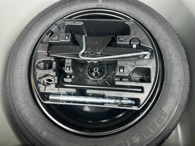 Vue rapprochée du pneu de secours noir d'une Peugeot 208 1.2 Hybrid 110ch GT, avec outils de changement rangés au centre.