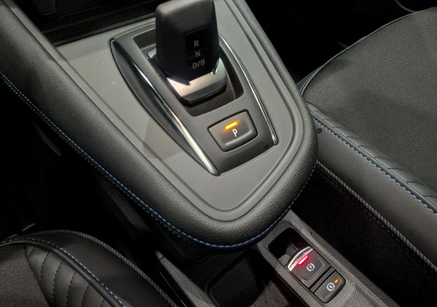 Gros plan sur la console centrale noire avec surpiqûres bleues du Renault Symbioz hybride, levier de vitesses et boutons de frein à main.