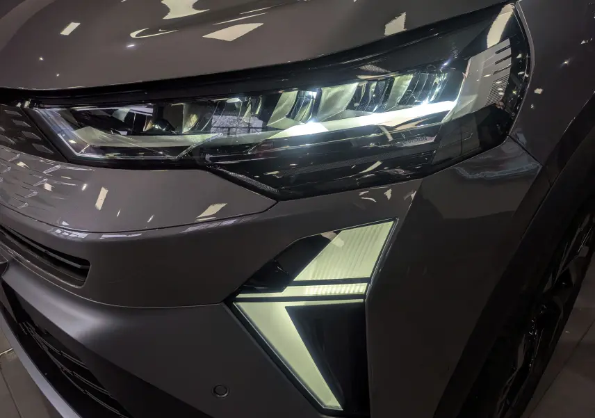 Gros plan sur le phare avant droit du Renault SYMBIOZ gris Cassiopé avec signature lumineuse en forme de flèche.