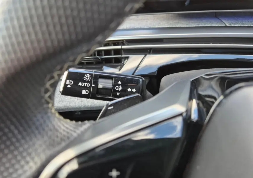 Gros plan sur la commande d’allumage automatique des feux derrière le volant du Peugeot 3008 Hybrid gris clair 2024.