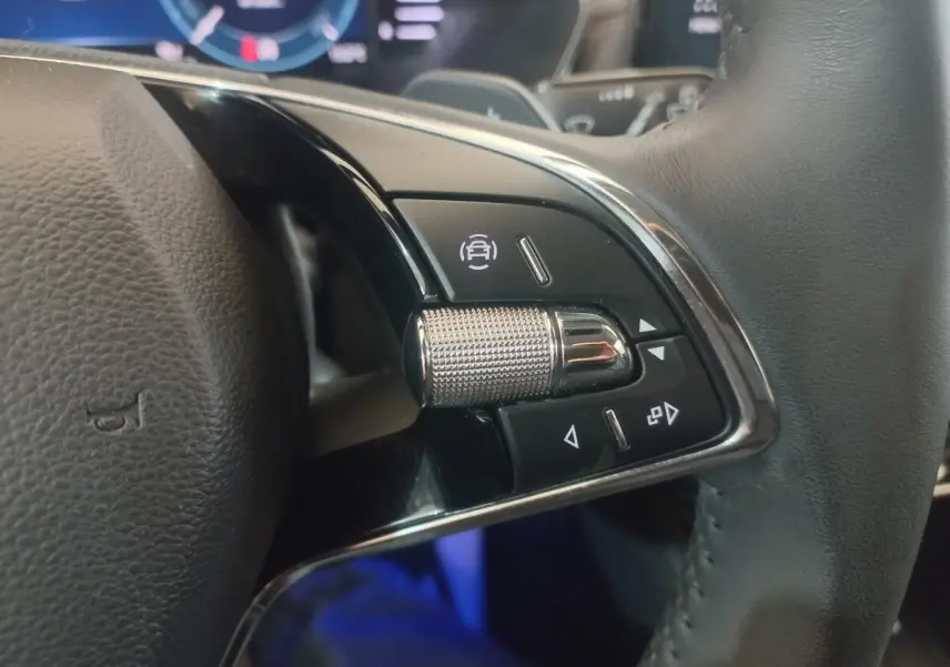 Gros plan sur les commandes multifonctions en alu et cuir du volant de la Skoda Octavia bleu, tableau de bord numérique en arrière-plan.