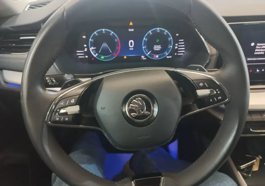 Vue rapprochée du volant cuir noir de la Skoda Octavia 2022 avec tableau de bord numérique et éclairage d’ambiance bleu.