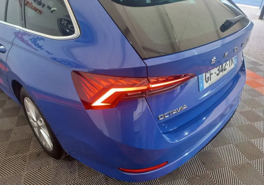 Vue 3/4 arrière droite d'une Skoda Octavia bleue 2022 avec feux arrière LED allumés et logo visible.