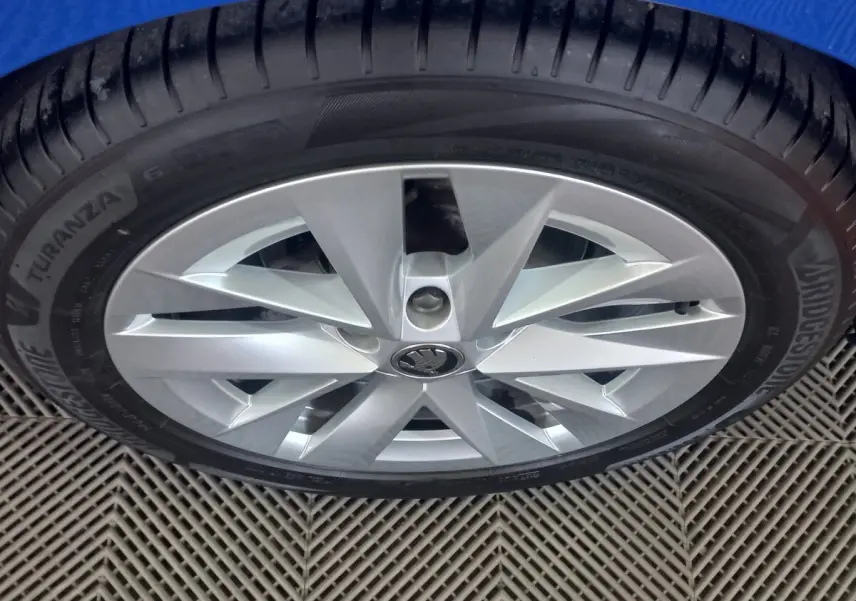 Gros plan sur la roue avant droite avec jante argentée et logo ŠKODA au centre sur fond bleu.