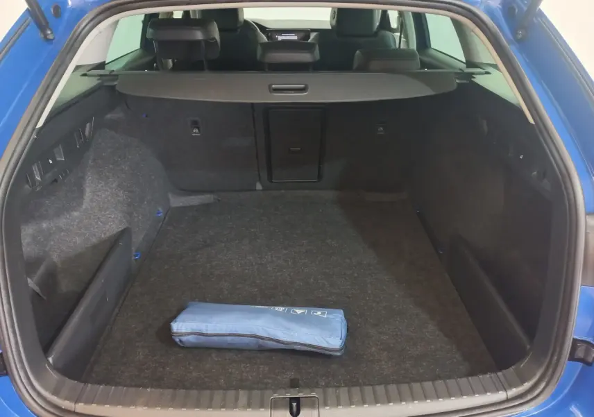 Coffre ouvert vu de l'arrière d'une Skoda Octavia bleu 2022, avec tapis gris et trousse bleue posée au centre.