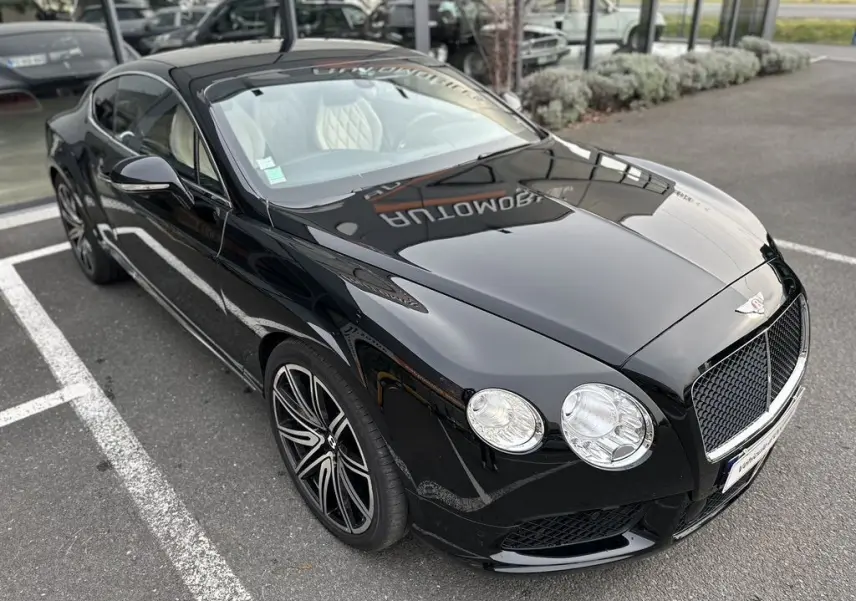 Bentley Continental GT Mulliner noire vue en 3/4 avant droit, avec jantes sport et intérieur clair visible.