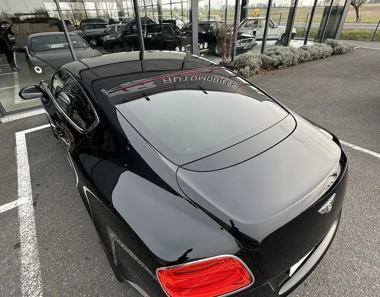 Vue 3/4 arrière droite d'une Bentley Continental GT Mulliner noire brillante, avec feux arrière rouges et logo Bentley visible.