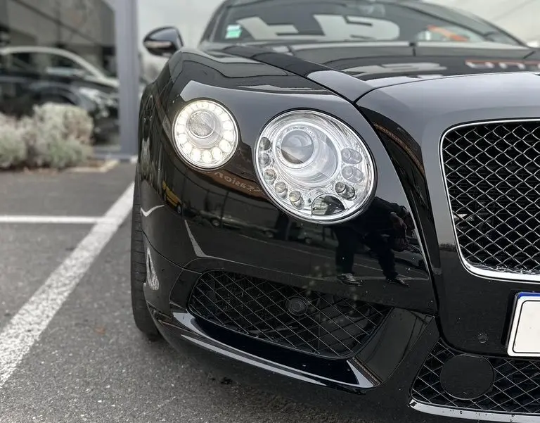 Vue rapprochée 3/4 avant gauche du Bentley Continental GT Mulliner noire, mettant en valeur ses phares ronds distinctifs.