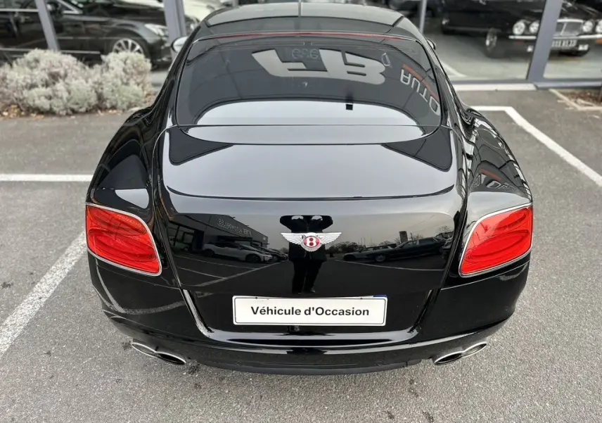 Vue arrière d'une Bentley Continental GT 4.0 V8 Mulliner noire de 2013 avec feux rouges et double sortie d'échappement chromée.