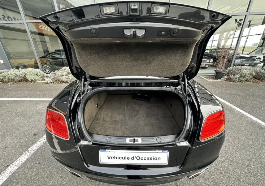 Vue arrière d'une Bentley Continental GT Mulliner noire de 2013 avec coffre ouvert et intérieur de coffre beige visible.