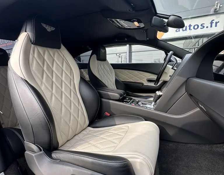 Intérieur de Bentley Continental GT 2013, vue côté gauche sur sièges cuir noir et beige matelassé avec logo Mulliner brodé.