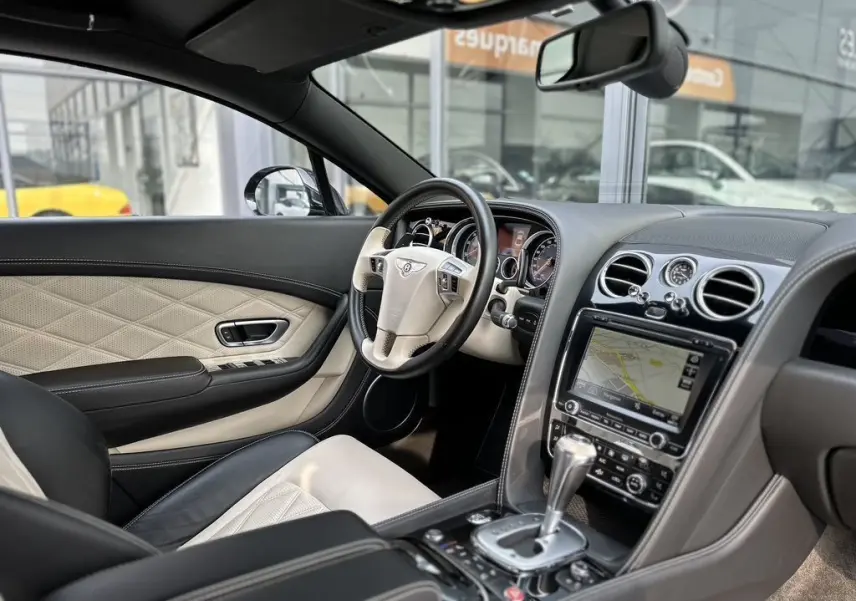 Intérieur beige et noir de la Bentley Continental GT Mulliner 2013, vue côté conducteur avec tableau de bord et console centrale.