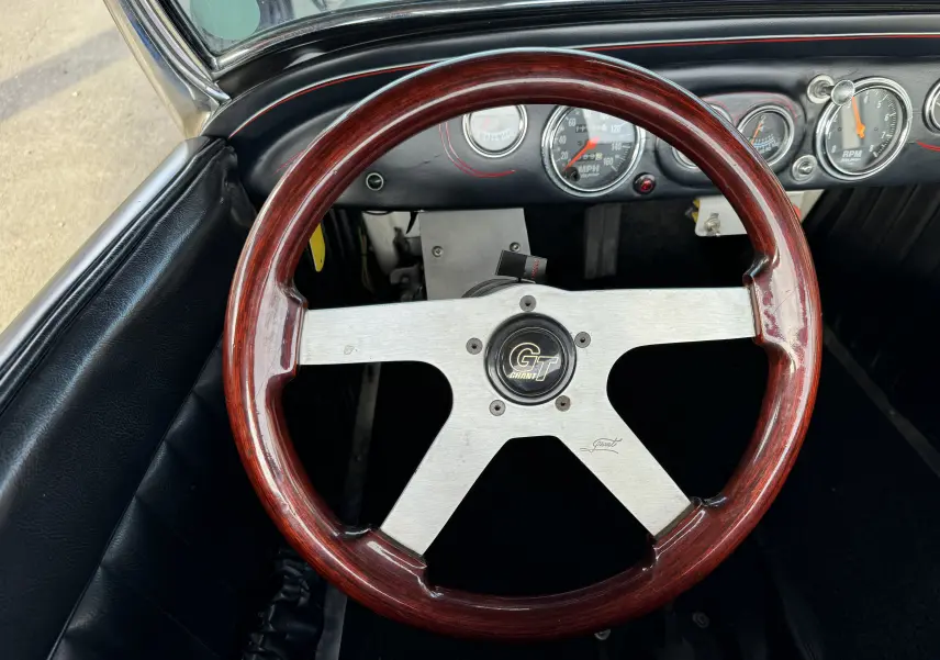 Vue rapprochée du volant en bois GT Grant du Ford T Hot Rod 1923, avec tableau de bord noir et compteurs ronds visibles.