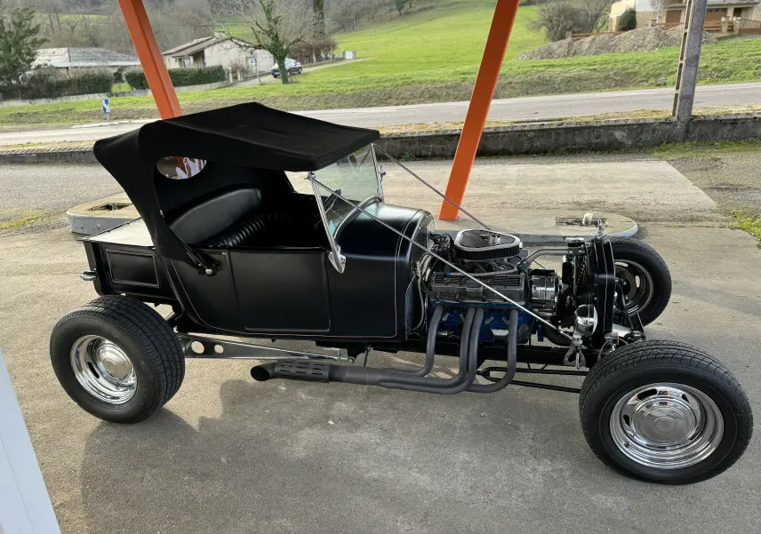 Ford T Hot Rod V8 noir vue de profil côté gauche, capote noire relevée et moteur V8 apparent avec échappements latéraux.