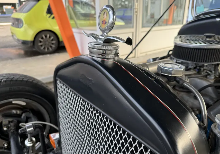 Gros plan sur la calandre noire du Ford T Hot Rod 1923 avec capuchon de radiateur orné et liseré rouge fin.