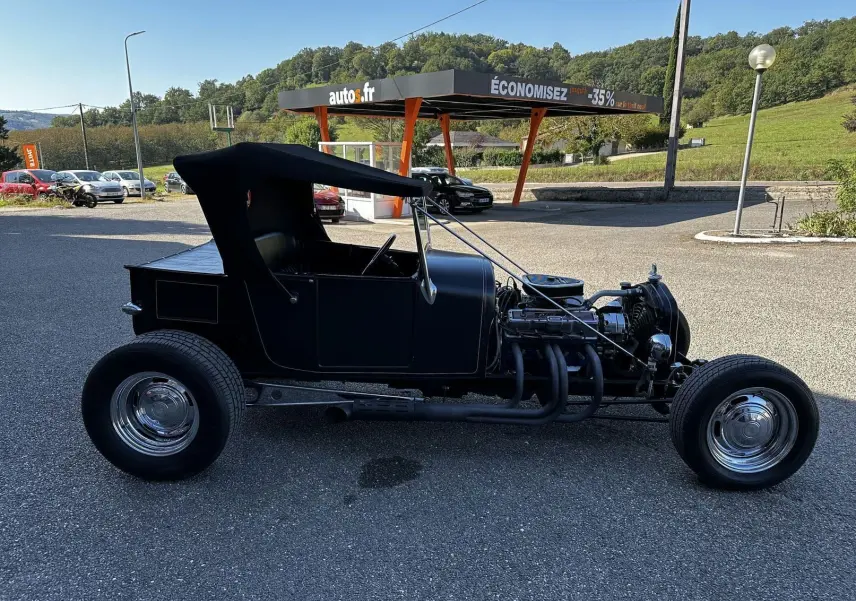 Profil côté gauche d'une Ford T Hot Rod V8 noire de 1923 avec toit décapotable en position haute et moteur apparent.