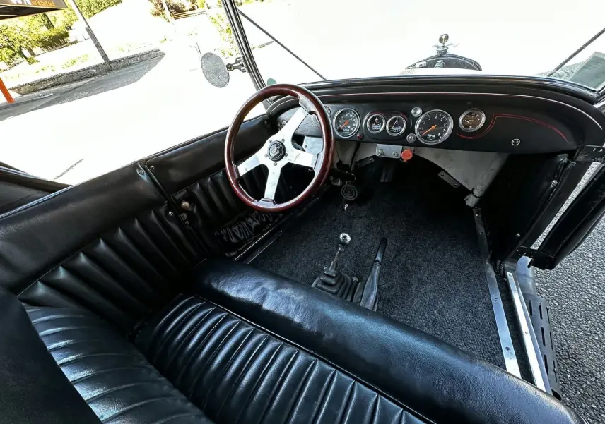 Vue intérieure côté conducteur de la Ford T Hot Rod 1923 noire, volant bois GT et tableau de bord avec compteurs ronds.