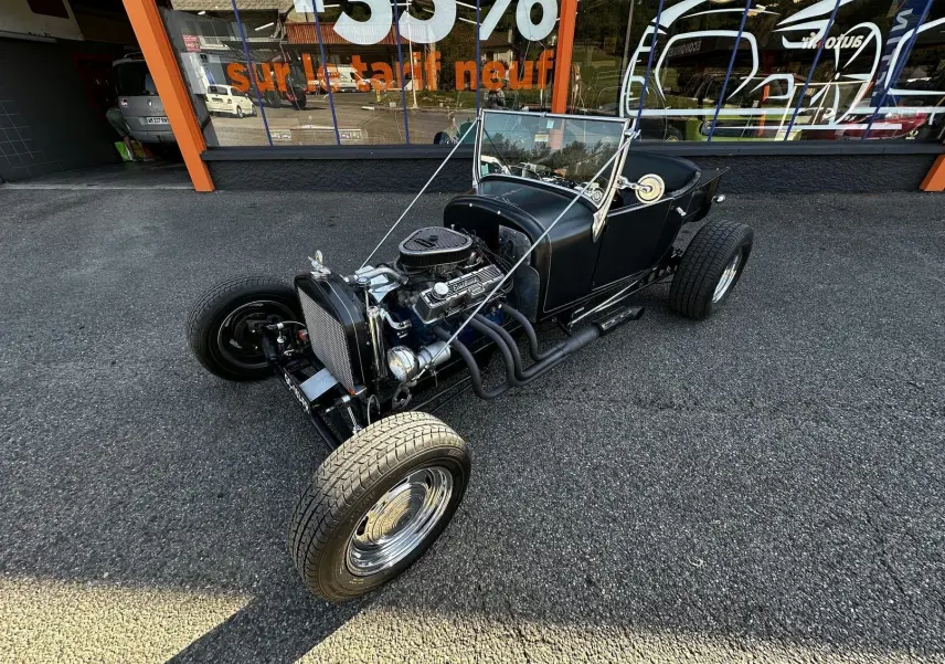 Ford T Hot Rod V8 noir vue 3/4 avant droit, capote décapotée et moteur V8 apparent avec détails chromés.