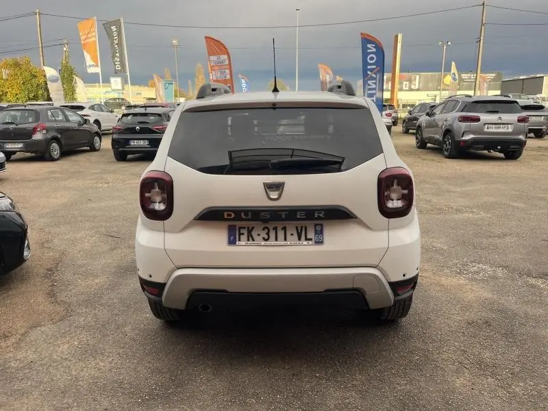 Vue arrière d'un Dacia Duster blanc Glacier 2019 avec feux arrière carrés et barres de toit visibles.