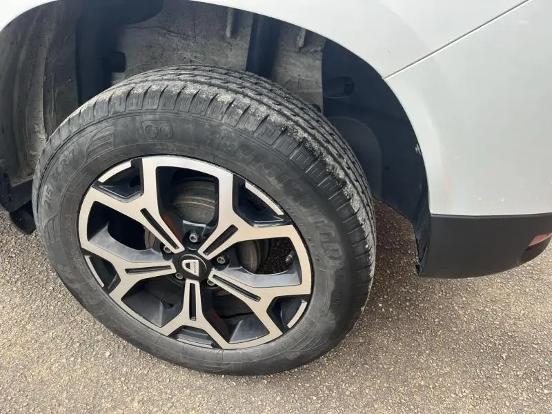 Gros plan sur la roue arrière droite du Dacia Duster blanc Glacier avec jante alliage noire et argentée.