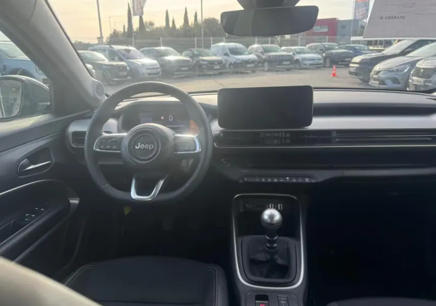 Vue intérieure avant du Jeep Avenger gris 2025, mettant en valeur le volant, la boîte manuelle et l'écran central.