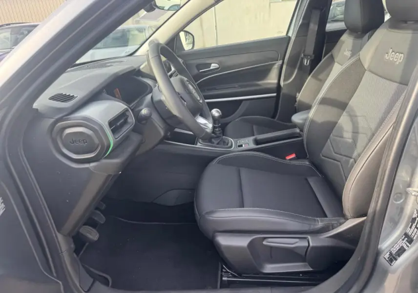 Vue intérieure côté conducteur du Jeep Avenger gris 2025, avec sièges noirs marqués Jeep et boîte manuelle visible.
