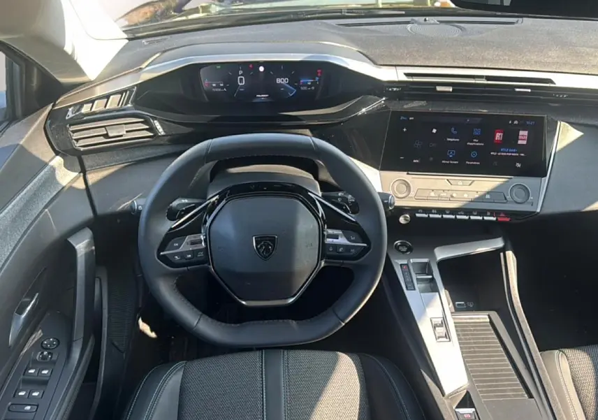 Vue intérieure du poste de conduite de la Peugeot 308 2025, volant multifonction et écran tactile central visibles.