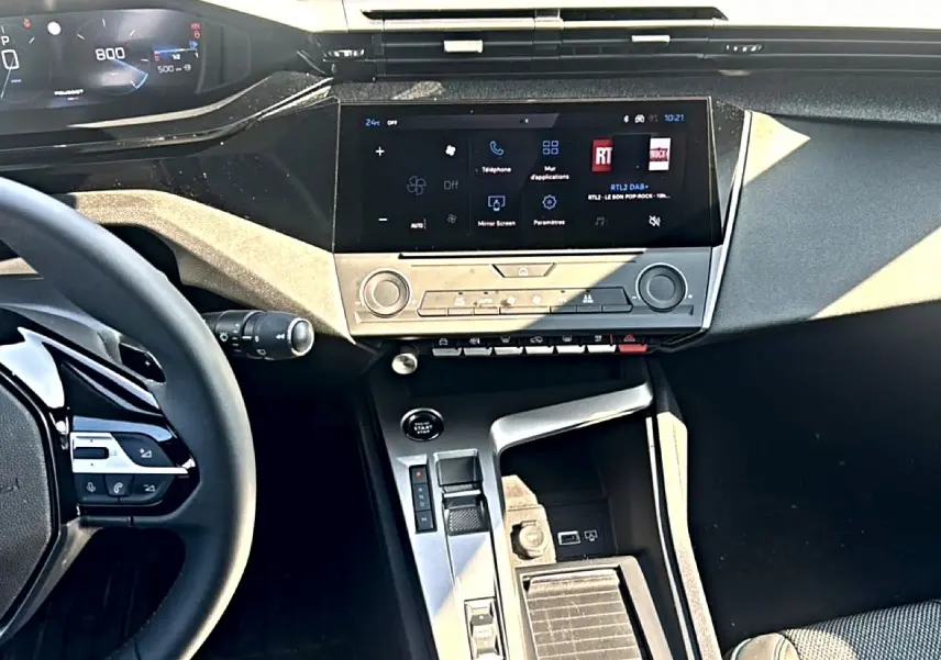 Vue intérieure de la Peugeot 308 2025, tableau de bord et console centrale avec écran tactile et volant multifonction.