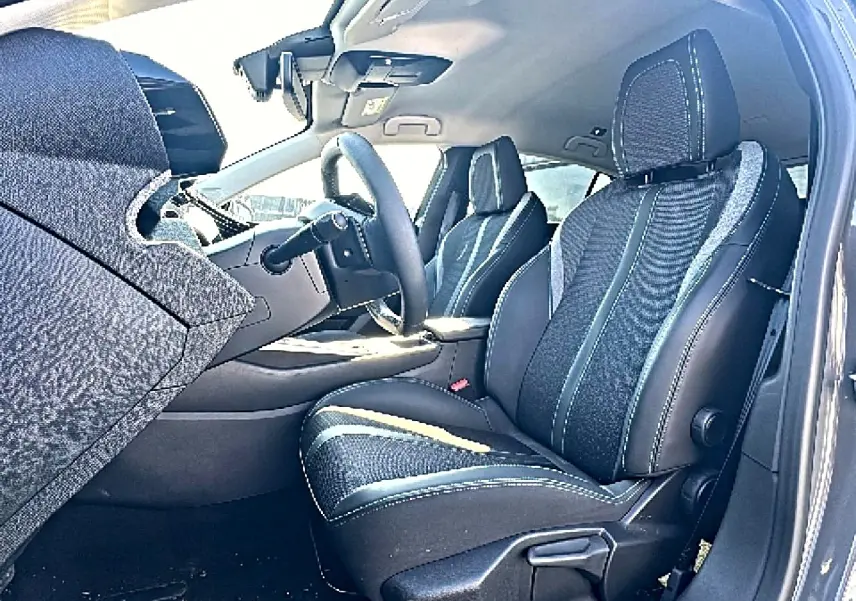 Vue intérieure côté conducteur de la Peugeot 308 2025, sièges tissu noir avec surpiqûres contrastantes et accoudoir central.