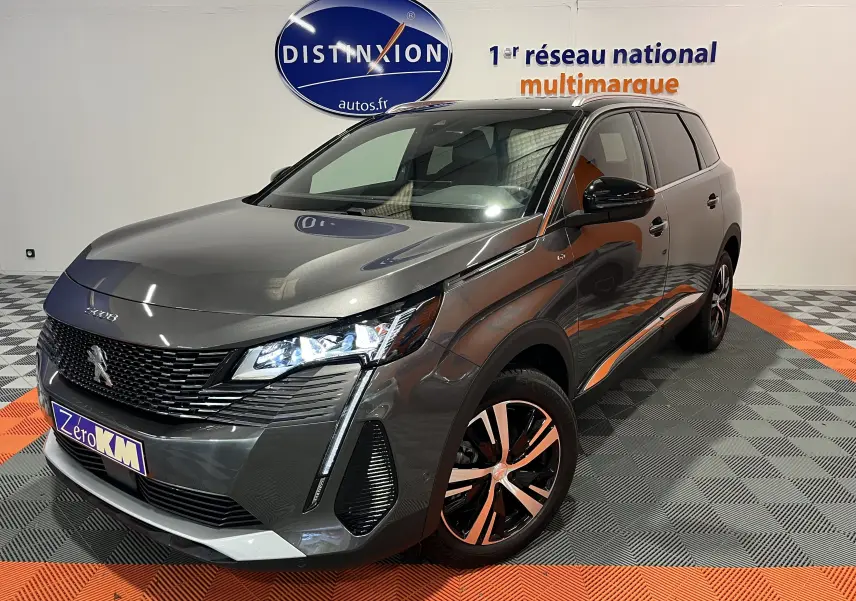 Vue 3/4 avant droit d'un Peugeot 5008 gris platinium 2024 avec phares LED et jantes alliage bicolores.