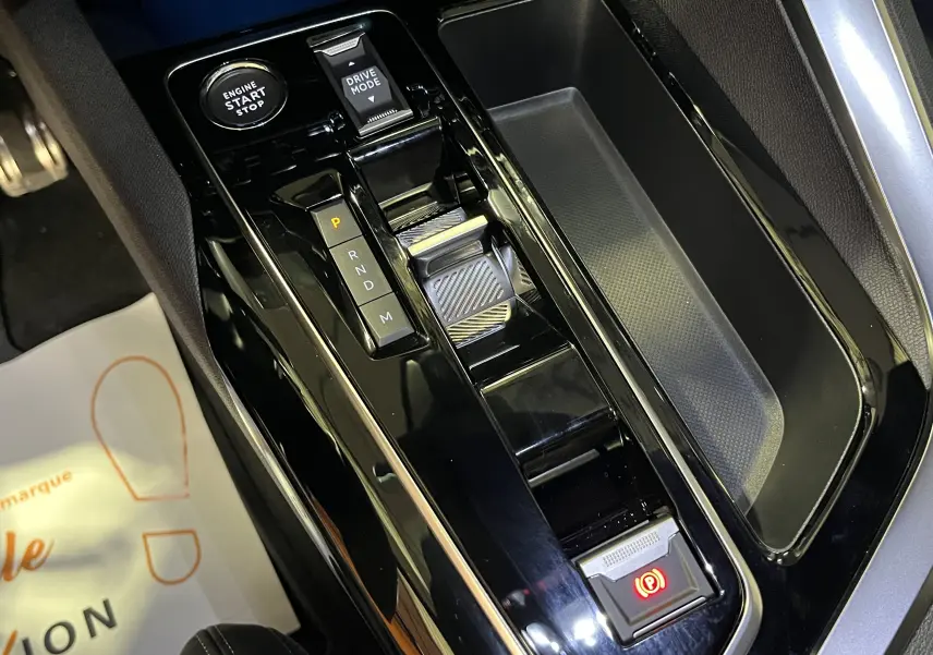 Vue rapprochée de la console centrale noire brillante du Peugeot 5008 2024, avec levier de vitesse automatique et bouton start-stop.