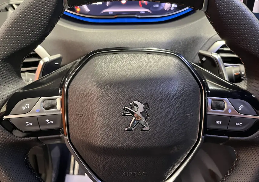 Gros plan sur le volant cuir perforé du Peugeot 5008 2024 avec commandes intégrées et logo lion central chrome.