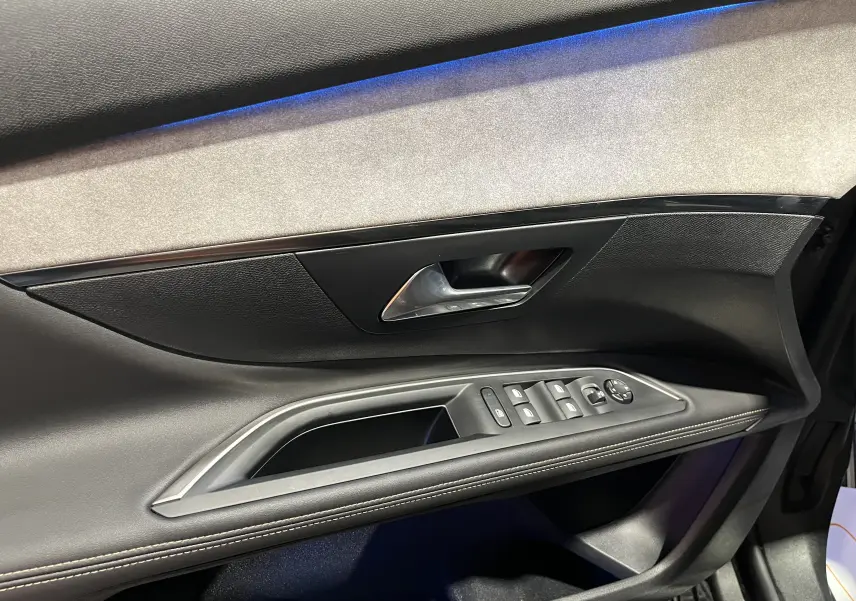Intérieur côté gauche de la porte avant du Peugeot 5008 GT 2024, avec garniture noire et éclairage d'ambiance bleu.