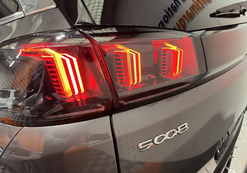 Gros plan sur le feu arrière droit rouge vif du Peugeot 5008 gris platinium 2024, avec logo visible sur la carrosserie.