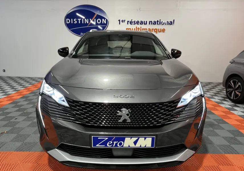 Vue frontale d'un Peugeot 5008 gris platinium avec phares LED allumés dans un showroom.