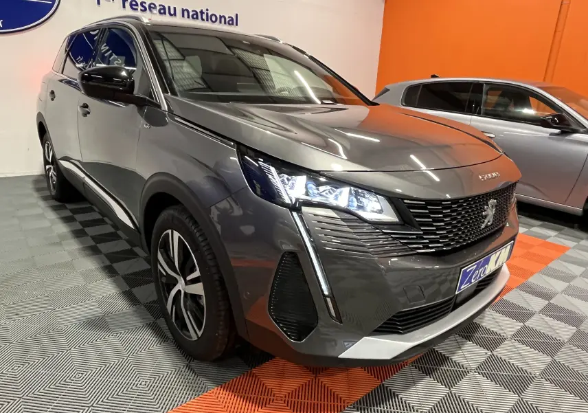 Peugeot 5008 BlueHDi 130 EAT8 GT gris platinium en 3/4 avant droit, phares LED allumés, intérieur showroom.